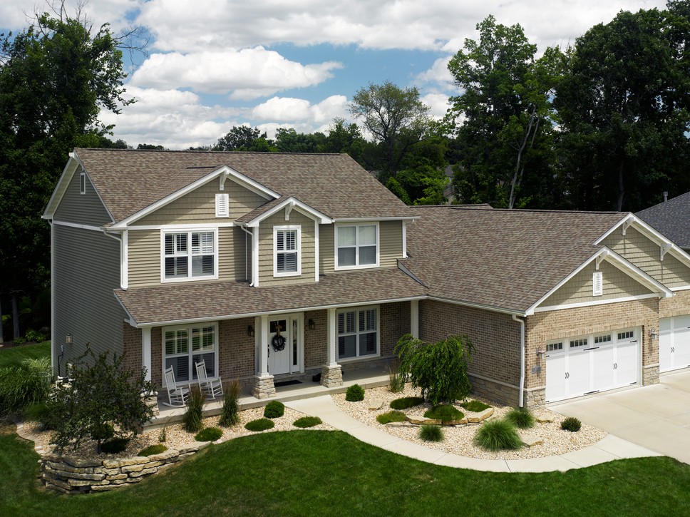A vinyl-siding and brick home with a newly replaced roof that has various asphalt- colored shingles.