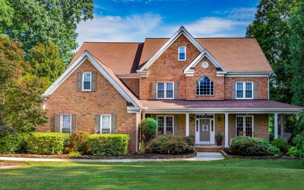 The front of a red-brick traditional-style home with brown window shutters, a brown entry door, and
